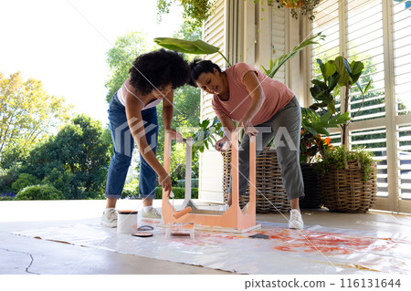 Biracial mother and adult daughter are painting a chair pink outside at home as an upcycling project Biracial mother and adult daughter are painting a chair pink outside at home as an upcycling project 116131644