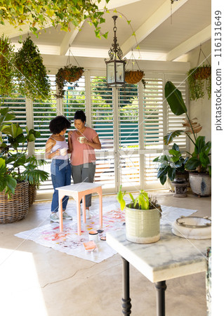 Biracial mother and adult daughter painting furniture together at home in an upcycling project 116131649