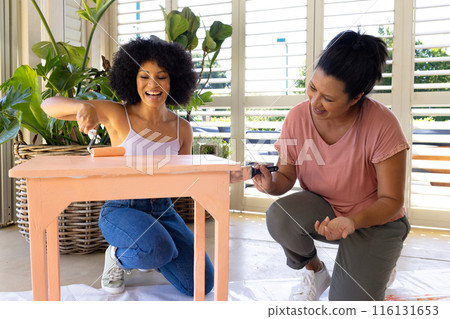 Biracial mother and adult daughter painting furniture together at home in an upcycling project 116131653