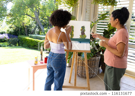 Biracial mother and adult daughter are painting outside, surrounded by greenery, at home Biracial mother and adult daughter are painting outside, surrounded by greenery, at home 116131677