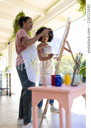 Mother and Daughter, mature biracial woman painting with young biracial woman outdoors at home 116131682
