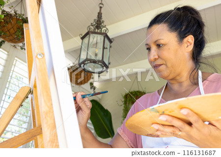 Mature biracial woman painting on canvas at home, focused on art Mature biracial woman painting on canvas at home, focused on art 116131687