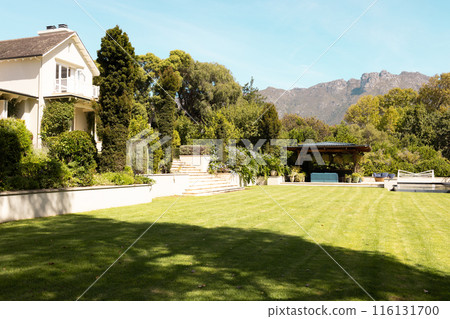 Lush green lawn stretches in front of large house with mountains behind, at home 116131700