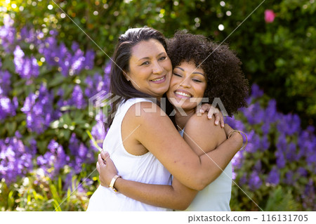 Mother and Daughter, mature biracial woman and young biracial woman hugging in garden at home 116131705