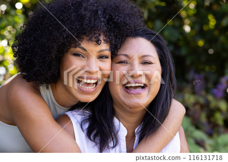Biracial mother and adult daughter are laughing together outdoors at home in the garden 116131718