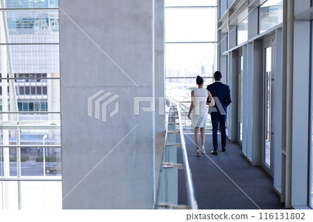Biracial colleagues walking down office hallway 116131802