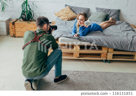 charming cool fair-haired woman with a white camera having a rest on the bed 116131851