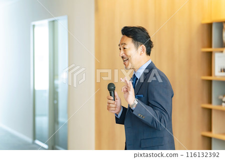 A middle-aged man giving a speech with a microphone in the lobby 116132392