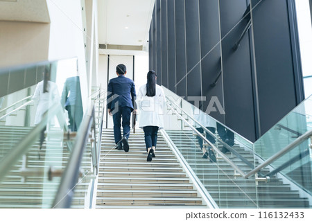 A group of businessmen and engineers in white coats climbing the stairs 116132433