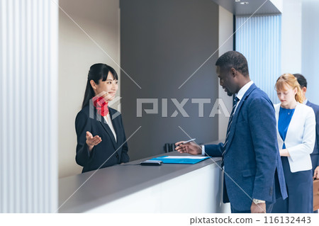 Multinational people checking in at a hotel front desk Multinational people checking in at a hotel front desk 116132443