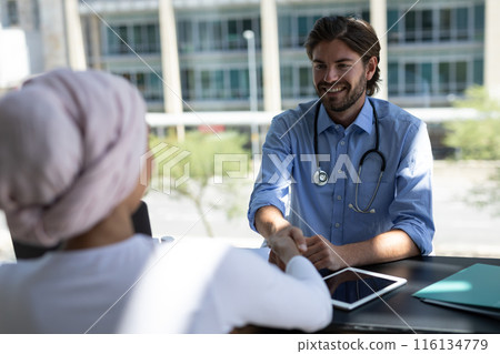 A Caucasian male doctor wearing blue shirt and stethoscope is talking to a patient 116134779