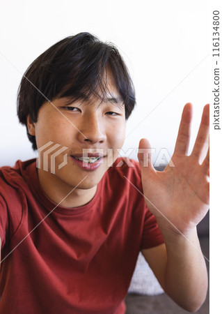 Asian teenage boy waving during a video call at home, sitting indoors Asian teenage boy waving during a video call at home, sitting indoors 116134800