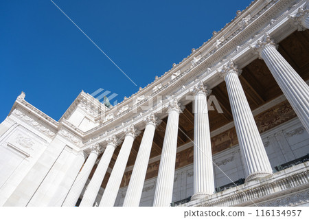A low-angle view of the white marble columns of the Vittoriano monument in Rome, Italy, against a clear blue sky. 116134957