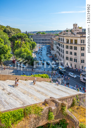 A view from above of the staircase leading to the Basilica of Saint Mary of the Altar in Heaven in Rome, Italy. Tourists can be seen walking up the steps, and cars are driving on the street below. 116134962