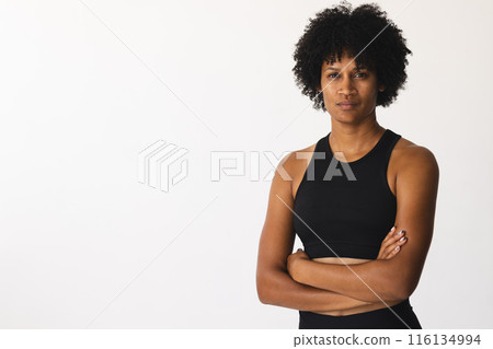 Biracial female yoga instructor standing in studio with arms crossed, looking serious, copy space 116134994