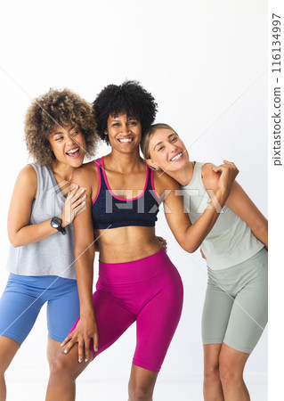 Three diverse women are posing together in studio, smiling in fitness attire, copy space 116134997
