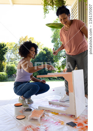 Biracial mother and adult daughter painting furniture outdoors at home in an upcycling project 116135007