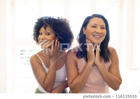 Biracial mother and adult daughter are standing, touching faces, smiling at home, copy space Biracial mother and adult daughter are standing, touching faces, smiling at home, copy space 116135010