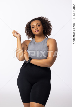 Biracial young female plus size model with curly brown hair standing confidently on white background Biracial young female plus size model with curly brown hair standing confidently on white background 116135064