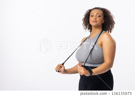 Biracial young female plus size model holding resistance band, looking confident on white background 116135075