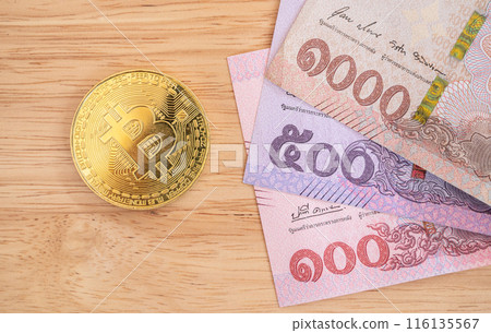 A Bitcoin token with Thai Baht banknotes on wooden table. Conceptual shot of business and financial items for trading. A Bitcoin token with Thai Baht banknotes on wooden table. Conceptual shot of business and financial items for trading. 116135567