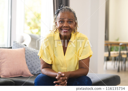 African American senior woman sitting at home, wearing a yellow shirt and jeans 116135734
