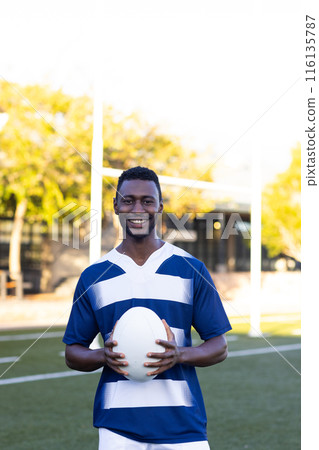 African American young male athlete holding a rugby ball, standing on field outdoors, copy space African American young male athlete holding a rugby ball, standing on field outdoors, copy space 116135787