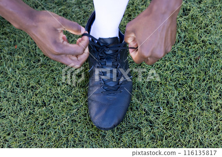 African American young male athlete tying black shoe laces on a grass field outdoors 116135817