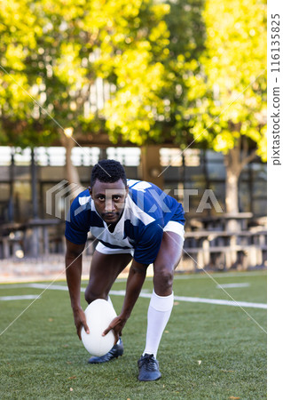 African American young male athlete placing rugby ball on field, looking focused, copy space 116135825