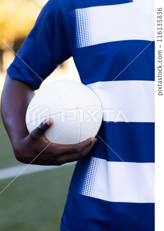 African American young male athlete holding a rugby ball, ready to play on the field outdoors African American young male athlete holding a rugby ball, ready to play on the field outdoors 116135836