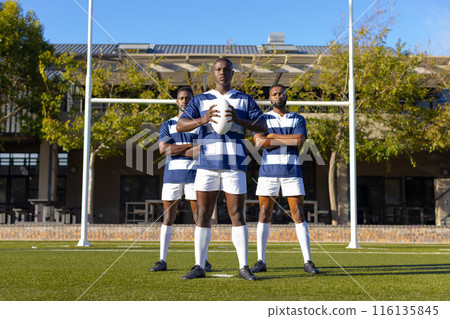 Three African American young male athletes holding a rugby ball on a field outdoors 116135845