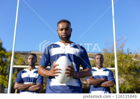 Three African American young male athletes holding a rugby ball, standing on field outdoors 116135849