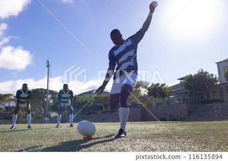 Three African American young male athletes playing rugby on a sunny field, copy space Three African American young male athletes playing rugby on a sunny field, copy space 116135894