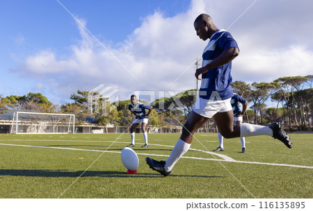 Three African American young male athletes training with a rugby ball on a field outdoors Three African American young male athletes training with a rugby ball on a field outdoors 116135895