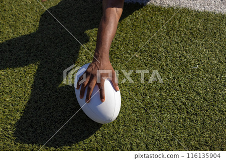 African American young male athlete holding a rugby ball on grass, copy space 116135904