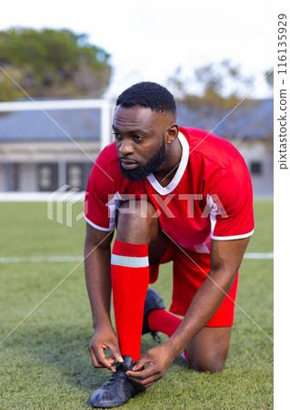 African American young male athlete tying shoelaces on a soccer field outdoors African American young male athlete tying shoelaces on a soccer field outdoors 116135929