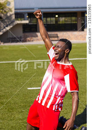 African American young male athlete in red & white jersey celebrates on field outdoors, copy space African American young male athlete in red & white jersey celebrates on field outdoors, copy space 116135965