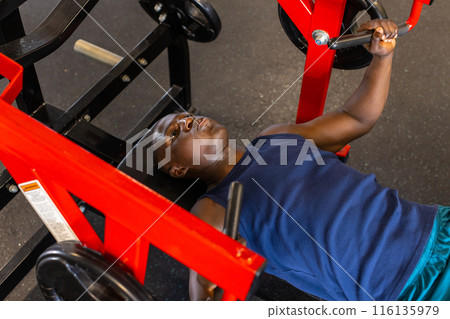An African American young male athlete is training with a chest press machine in a gym 116135979