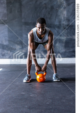 African American young male athlete, a fitness model lifting kettlebell in gym, focusing on exercise African American young male athlete, a fitness model lifting kettlebell in gym, focusing on exercise 116135989
