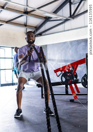 Two African American young male athletes are training with battle ropes in gym 116135995