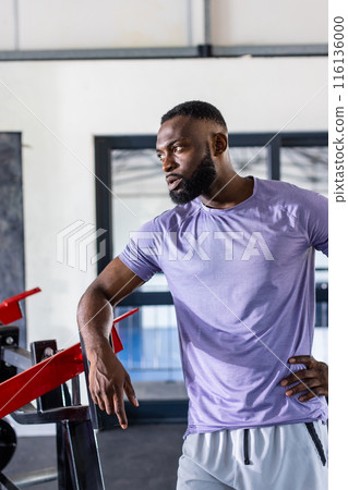 African American young male athlete leaning on gym equipment in gym, taking a break African American young male athlete leaning on gym equipment in gym, taking a break 116136000