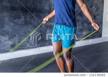 An African American young male athlete is jumping rope in a gym, wearing sportswear, copy space An African American young male athlete is jumping rope in a gym, wearing sportswear, copy space 116136002