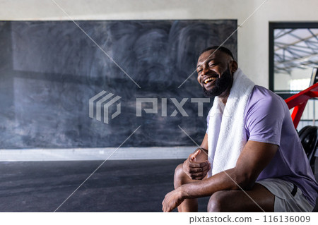 African American young male athlete and fitness model sitting, laughing in gym, copy space 116136009