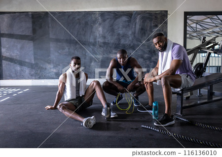 Three African American young male athletes are resting in gym, copy space 116136010
