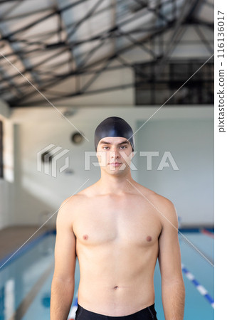 Caucasian young male swimmer standing by pool indoors, looking at camera, copy space Caucasian young male swimmer standing by pool indoors, looking at camera, copy space 116136017