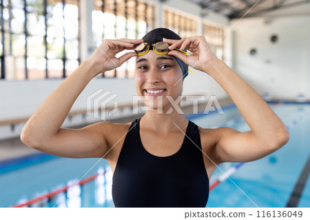 Biracial young female swimmer adjusting goggles in pool area indoors Biracial young female swimmer adjusting goggles in pool area indoors 116136049
