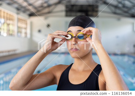 Young biracial female swimmer adjusting goggles at an indoor pool Young biracial female swimmer adjusting goggles at an indoor pool 116136054