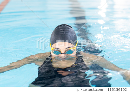 A biracial young female swimmer wearing goggles is swimming indoors A biracial young female swimmer wearing goggles is swimming indoors 116136102