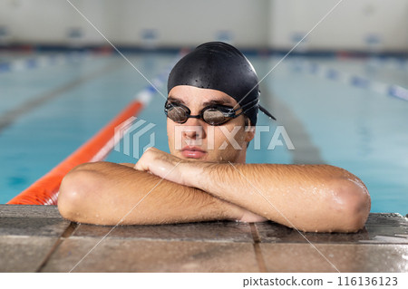 Caucasian young male swimmer resting at pool edge indoors, looking forward Caucasian young male swimmer resting at pool edge indoors, looking forward 116136123