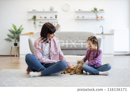 Mother and daughter petting cat in cozy living room 116136171